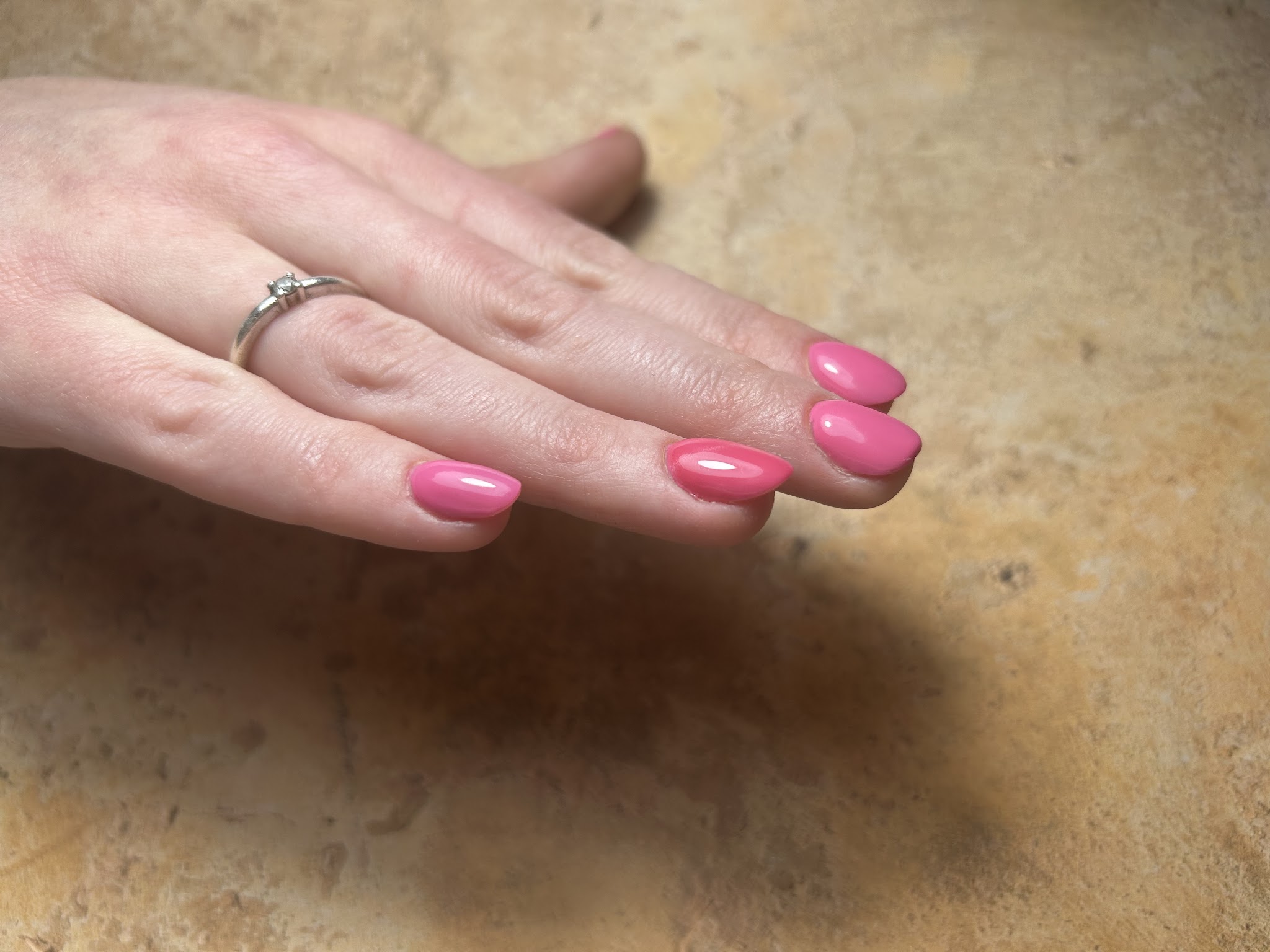Felroze glanzende nagels, hand met ring op zandkleurige steen
