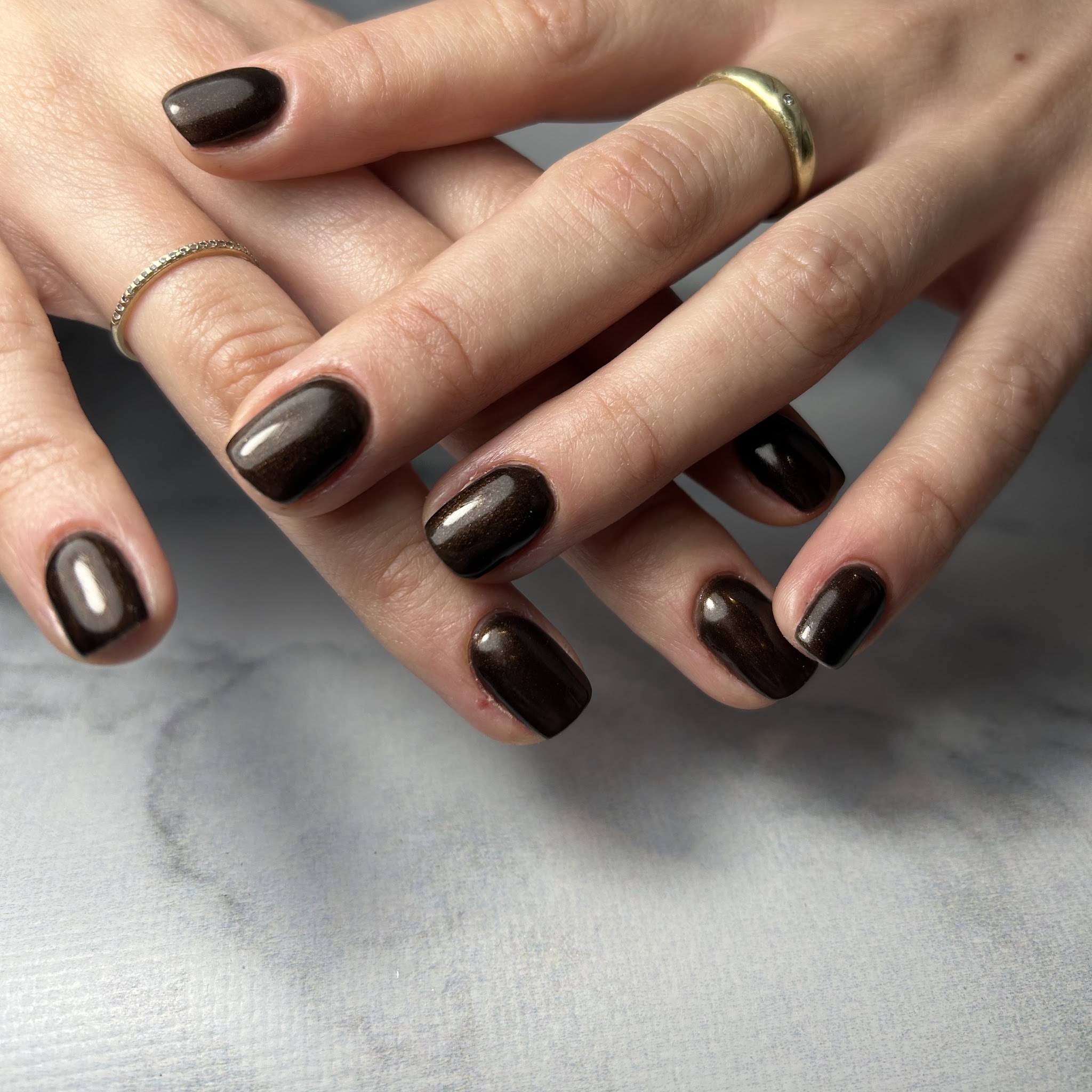 Diep chocoladebruine glanzende nagels op grijs marmer